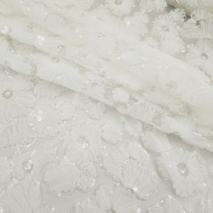 May include: White tulle fabric with a floral pattern and sequins. The fabric is sheer and has a delicate texture.