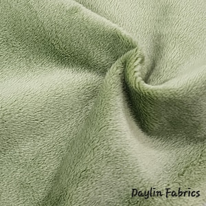 May include: Close-up of a soft, green fabric with a fuzzy texture. The fabric is folded and shows the pile of the material. The text "Daylin Fabrics" is visible in the bottom right corner of the image.