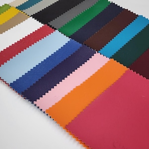 Puede incluir: Una colección de 20 muestras de tela en varios colores, incluyendo rojo, azul, verde, naranja y rosa. Las muestras están dispuestas en forma de abanico, con los bordes de cada muestra superpuestos ligeramente.