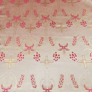 May include: Close-up of a fabric featuring a repeating pattern of crosses, wheat stalks, and floral elements in gold and pink. The fabric has a light pink background, suitable for religious garments or decor.