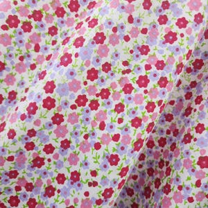 May include: White fabric with a small-scale floral print featuring pink, red, and purple flowers. The fabric is folded in half.