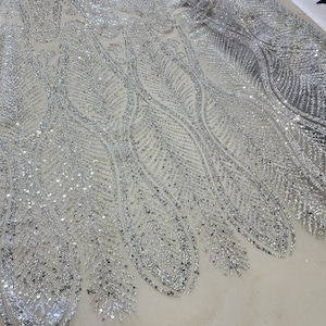 May include: Silver glitter fabric with a feather pattern. The fabric has a mesh backing and is ideal for adding sparkle to any project.