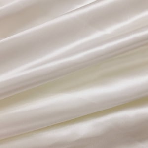 May include: Close-up of a smooth, white fabric with soft folds and a subtle sheen. The fabric has a luxurious and elegant appearance.