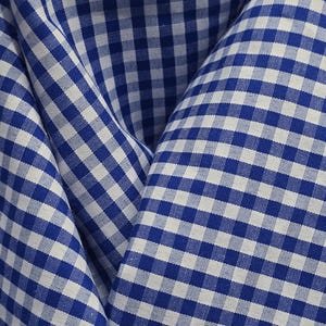 Puede incluir: Una tela con un patrón clásico de cuadros vichy en azul y blanco. El material está doblado para mostrar la textura y el diseño de cuadrícula consistente de los pequeños cuadrados alternos en la superficie del textil en un patrón repetitivo.