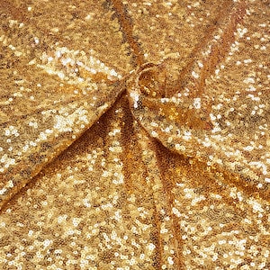 Op de afbeelding: Gouden paillettenstof met een textuur en een glinsterend oppervlak. De stof is in het midden gevouwen, wat een dramatisch effect creëert.