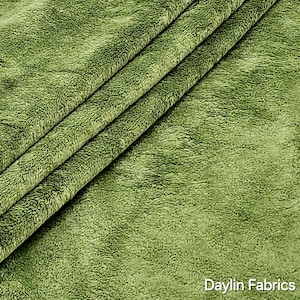 Könnte beinhalten: Nahaufnahme eines weichen, grünen Stoffes mit einer flauschigen Textur. Der Stoff ist dreifach gefaltet und zeigt die Textur aus verschiedenen Blickwinkeln. Der Text "Daylin Fabrics" ist in der rechten unteren Ecke sichtbar.