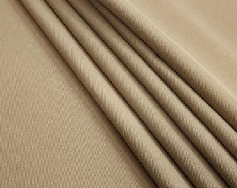 May include: Close-up of a beige fabric with a subtle ribbed texture. The fabric is folded in several layers, showcasing its drape and softness. The text "Paglin Fabrics" is visible in the bottom right corner.