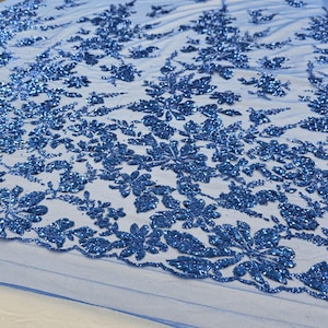 Puede incluir: Tela de encaje floral azul con purpurina. La tela tiene un delicado patrón floral con un acabado brillante de purpurina azul.