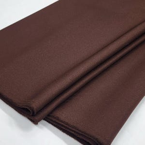 May include: A close-up of a brown fabric with a smooth, slightly shiny texture. The fabric is folded in half, showing the edges.