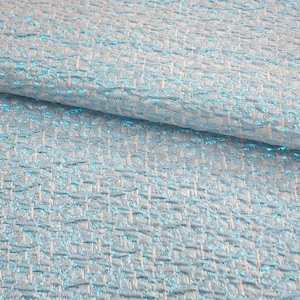 May include: A close-up of a light blue fabric with a woven pattern. The fabric has a subtle shimmer and a textured surface.