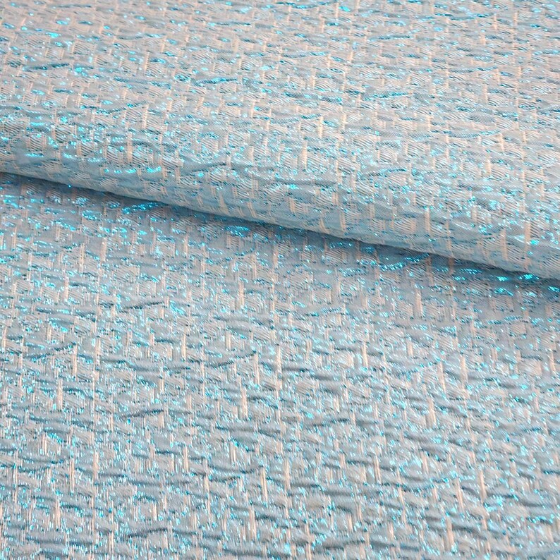 May include: A close-up of a light blue fabric with a woven pattern. The fabric has a subtle shimmer and a textured surface.