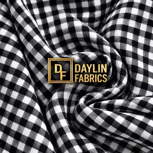 Pode incluir: Um tecido xadrez vichy em preto e branco com um padrão de quadrados pequenos, apresentando dobras e drapeados. Um logótipo quadrado dourado com as letras DF e o texto DAYLIN FABRICS está centrado na superfície do tecido.