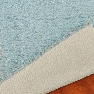 May include: Close-up of a light blue fabric with a textured woven pattern. The fabric is folded over, revealing a white backing.