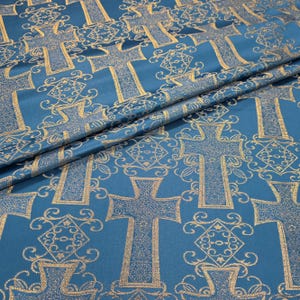 Puede incluir: Tela color turquesa con un patrón repetido de cruces doradas y diseños florales y geométricos ornamentados. La tela está doblada, mostrando la textura y el brillo del material. Adecuado para proyectos religiosos o decorativos.