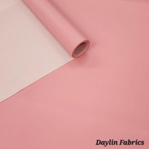 May include: A roll of pink faux leather fabric with a white backing. The fabric is rolled up and the white backing is visible. The text "Daylin Fabrics" is visible in the bottom right corner of the image.