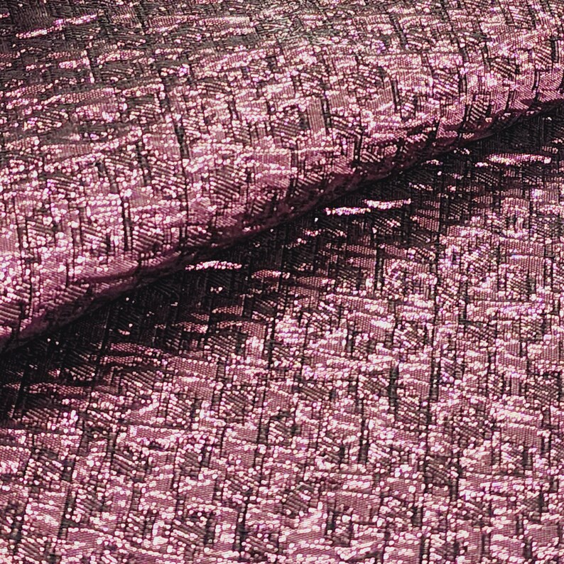 May include: Close-up of a pink and black textured fabric with a metallic sheen. The fabric has a woven pattern and a slightly iridescent finish.