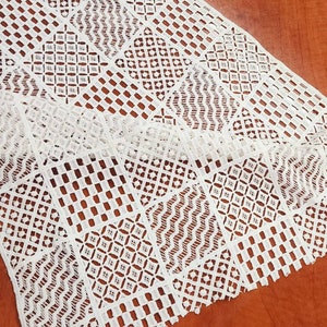 May include: White crochet lace trim with a geometric pattern. The lace is made of delicate, intricate stitches and has a soft, flowing texture.