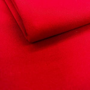 May include: A close-up shot of a vibrant red fabric, folded over to reveal a layered texture. The material appears soft and smooth, with a slight sheen. The color is a solid, saturated red, filling the frame.