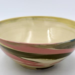 May include: A large, ceramic bowl with a cream-colored interior and a swirling pattern of pink, black, and gray stripes on the exterior.