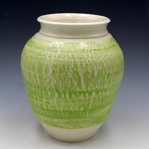 May include: A ceramic vase with a textured, lime green exterior and a cream-colored rim and base. The green surface has a vertical, striated pattern. The vase has a rounded body and a slightly flared opening.