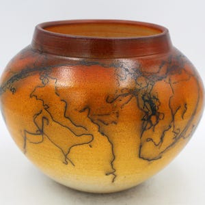 May include: A hand-painted ceramic vase with a brown, orange, and yellow glaze. The vase has a unique design of black lines that resemble a map or a network of veins.