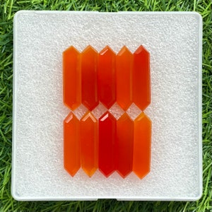 May include: A set of ten orange carnelian gemstone points in a white foam-lined box. The points are all approximately the same size and shape, with a pointed tip and a flat base.