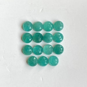 May include: A collection of 15 round, faceted, teal green gemstones. The gemstones are arranged in three rows of five.