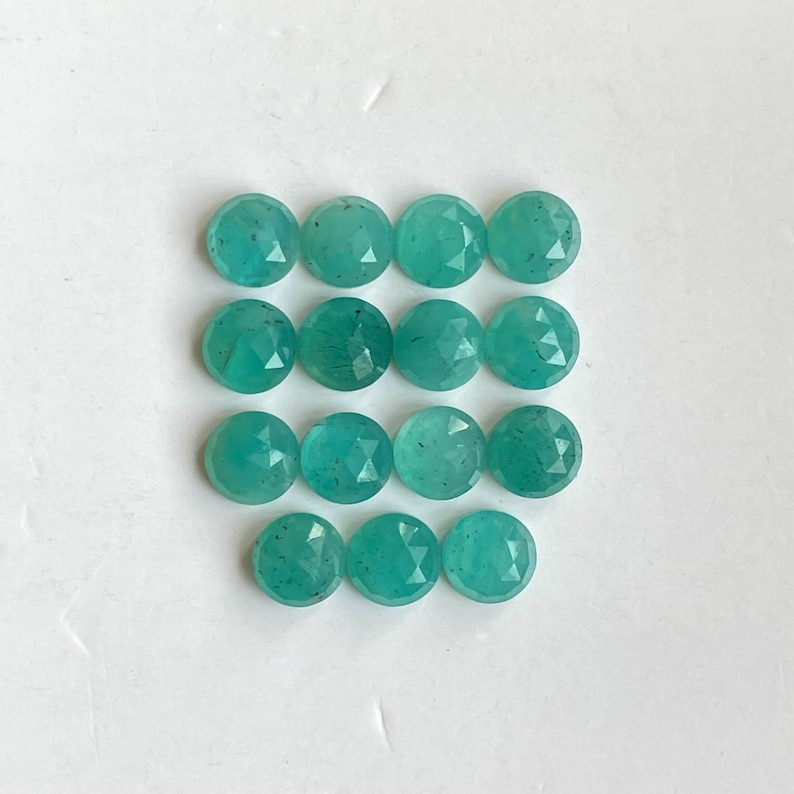 May include: A collection of 15 round, faceted, teal green gemstones. The gemstones are arranged in three rows of five.