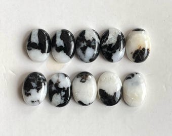 Könnte beinhalten: Zehn oval geformte Cabochons, angeordnet in zwei Reihen zu je fünf Stück. Jeder Stein hat eine glatte, polierte Oberfläche mit einem ausgeprägten marmorierten Muster aus opakem Weiß und tiefem Schwarz, was einzigartige Kontraste erzeugt.