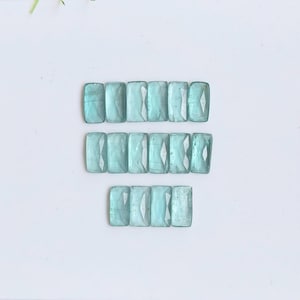 May include: Sixteen rectangular, faceted aquamarine gemstones arranged in three horizontal rows. Each stone features a light blue, translucent appearance with a polished surface and sharp, geometric edges, showcasing a consistent cut and clarity.