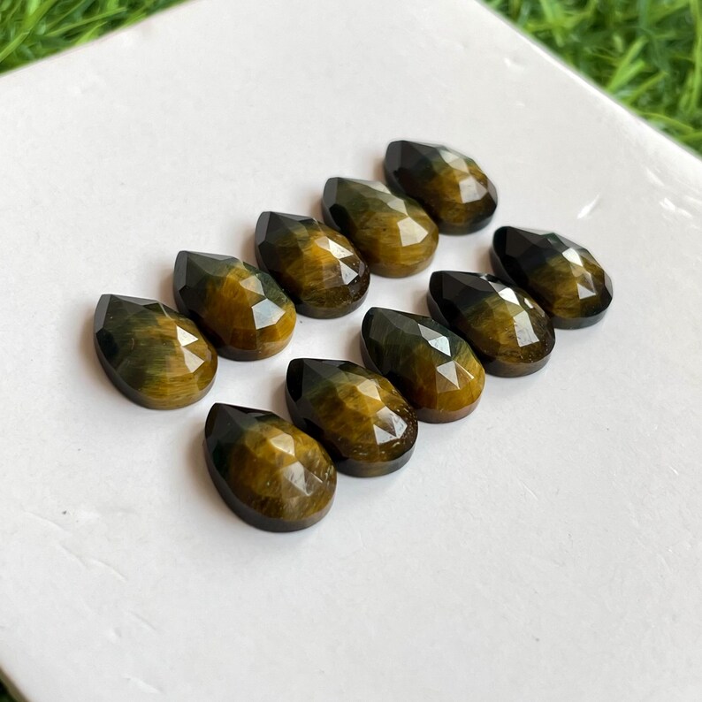 May include: Ten teardrop-shaped tiger's eye gemstones in shades of gold and green. The stones are faceted and have a pearlescent sheen.