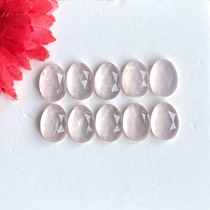 Könnte beinhalten: Zehn facettierte Rosenquarz-Edelsteine in hellrosa. Die Edelsteine sind oval geformt und haben eine glatte, polierte Oberfläche.