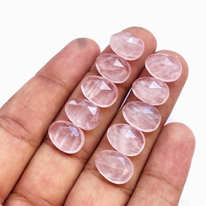 Könnte beinhalten: Zehn facettierte, ovale Rosenquarz-Edelsteine in verschiedenen Rosatönen. Die Steine sind glatt und poliert.