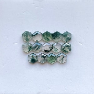 May include: A collection of twelve green moss agate cabochons, each cut into a hexagonal shape. The stones have a translucent, milky white base with green moss-like inclusions.