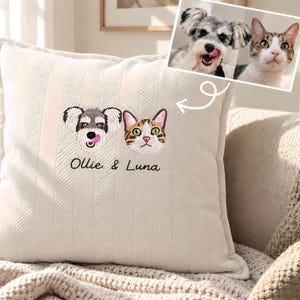 May include: A square off-white throw cushion with a textured herringbone pattern. The centre features custom embroidery of a dog and a cat face, with the text "Ollie & Luna" stitched in black thread below the animal portraits.