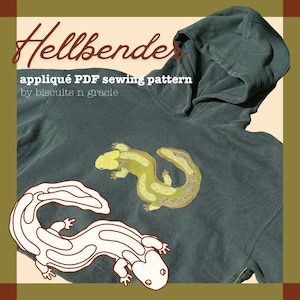 May include: A dark green hooded sweatshirt featuring a Hellbender appliqué PDF sewing pattern by biscuits n gracie. The hoodie displays a textured green salamander appliqué and a white line drawing of the same salamander shape.