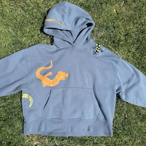 May include: A white ceramic mug with a black handle and the text "But First, Coffee" in a black, handwritten-style font. The mug is on a white surface.