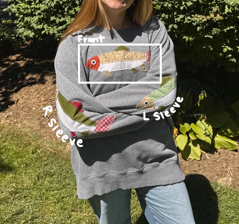 K&ouml;nnte beinhalten: Graues Sweatshirt mit Fischapplikationen auf der Vorderseite und den &Auml;rmeln. Die Vorderseite zeigt ein detailliertes Fischdesign mit roten, beigen und gr&uuml;nen Akzenten. &Auml;rmel mit Fisch- und Karopatch. Ein l&auml;ssiges, bequemes Kleidungsst&uuml;ck.