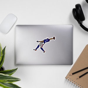 May include: A sticker depicting a cartoon football player in a blue and white uniform, mid-catch. The player is in a dynamic pose, reaching for the ball. The sticker is on a silver laptop, with a white mouse and black headphones visible.
