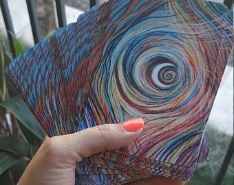 May include: A deck of colorful tarot cards with a swirling pattern and a crescent moon in the center. The cards are fanned out in a hand.