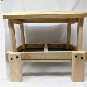 Puede incluir: Un comedero para p&aacute;jaros de madera con dos compartimentos y una parte superior plana. El comedero est&aacute; hecho de madera natural y tiene una mancha marr&oacute;n oscura. El comedero est&aacute; soportado por cuatro patas.