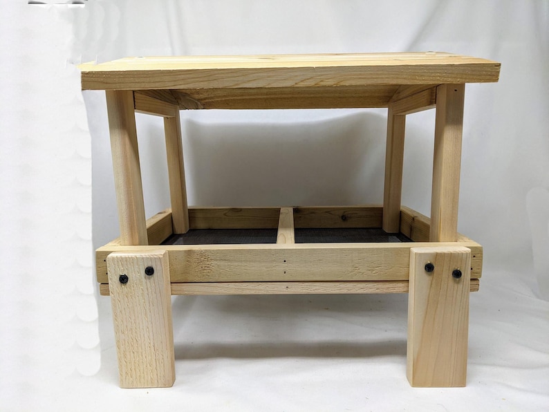 Puede incluir: Un comedero para p&aacute;jaros de madera con dos compartimentos y una parte superior plana. El comedero est&aacute; hecho de madera natural y tiene una mancha marr&oacute;n oscura. El comedero est&aacute; soportado por cuatro patas.