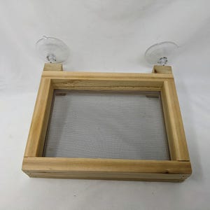 May include: A wooden frame with a mesh screen inside, attached to two suction cups. The frame is made of light wood and has a natural finish.