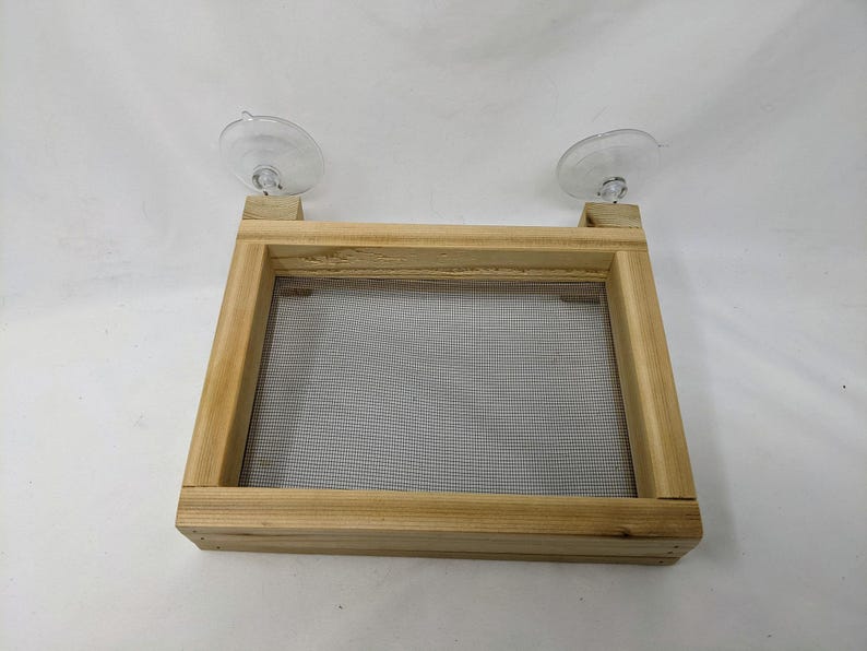 May include: A wooden frame with a mesh screen inside, attached to two suction cups. The frame is made of light wood and has a natural finish.