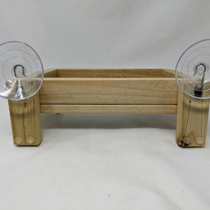 May include: A wooden bird feeder with two suction cups attached to the sides. The feeder is made of natural wood and has a rectangular shape.