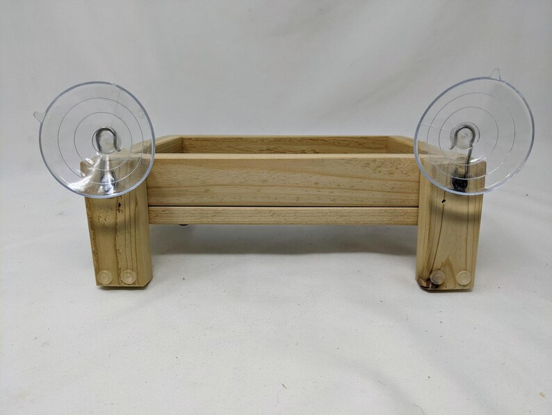 May include: A wooden bird feeder with two suction cups attached to the sides. The feeder is made of natural wood and has a rectangular shape.
