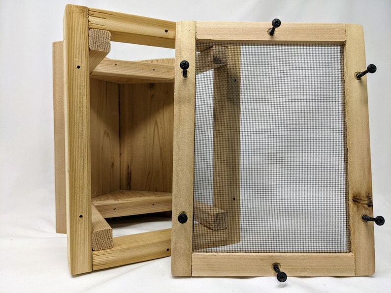 Puede incluir: Una casita de p&aacute;jaros de madera con un panel frontal extra&iacute;ble y una malla de alambre. La casita de p&aacute;jaros tiene una peque&ntilde;a plataforma de aterrizaje y un techo triangular.