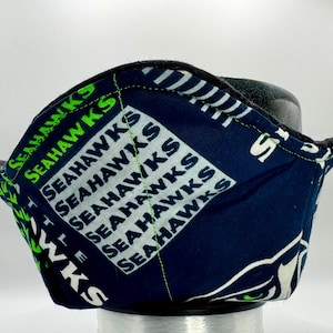Pode incluir: Uma proteção de tigela Seahawks azul marinho e verde. A proteção apresenta o nome da equipe em branco e verde, com um logotipo da equipe branco e verde. As bordas são pretas e as costuras são verdes.