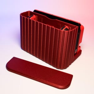 Puede incluir: Una maleta de transporte roja con un exterior acanalado y una tapa con bisagras. La maleta está abierta y revela un interior negro con dos mandos rojos.