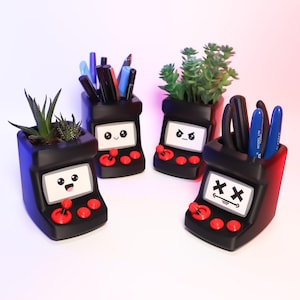 May include: Four black and red gaming console-shaped planters with different facial expressions. Two planters hold succulents, one holds pens and pencils, and one holds a set of tools.